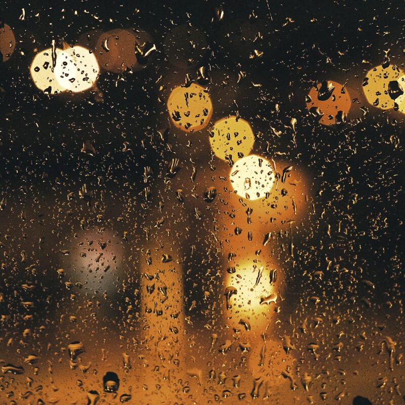 Verschwommene Lichter hinter einer Fensterscheibe mit Regentropfen