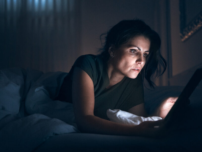 Eine Frau liegt im Bett und starrt in ihr Handy.