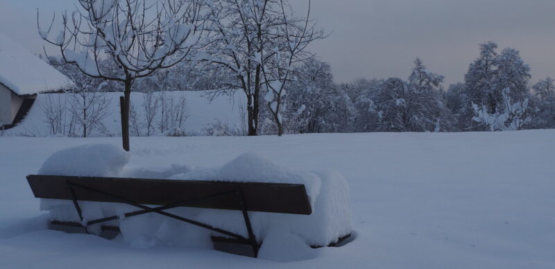 Verschneite Landschaft mit einer Bank im Vordergrund.